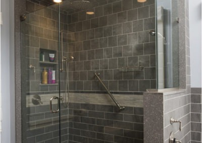 Abbey's custom design bathroom, step-in shower with porcelain & glass tile, quartz bench & trim, accessible grab bar and handheld showers.